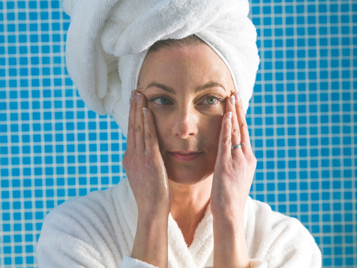 A woman applying natural face moisturizer with skincare products nearby.